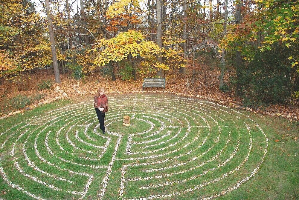 trees surrounding a labyrinth in the grass with a woman standing in the centre