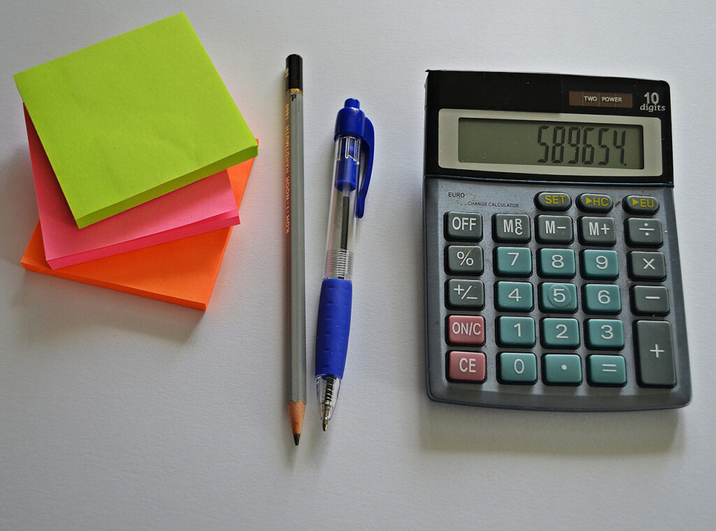 photo of bright coloured post it notes, a pencil, a pen and a calculator on a desk.