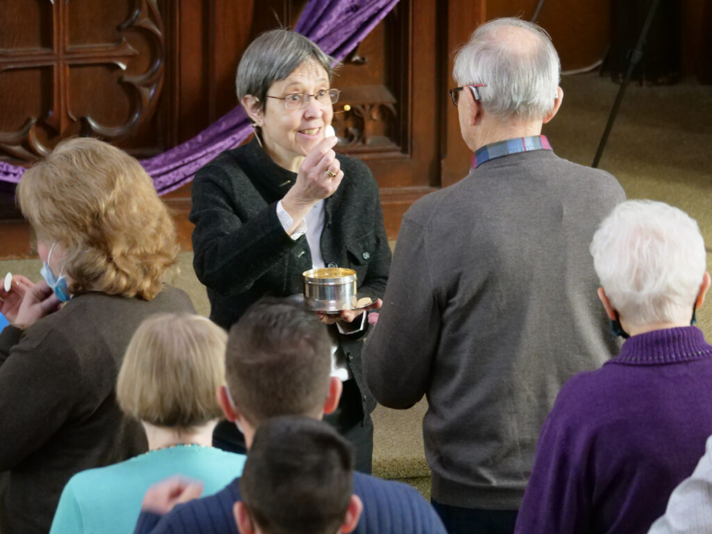 Pastor Daniella offering communion to a member of the Trinity Lutheran church congregation with other people